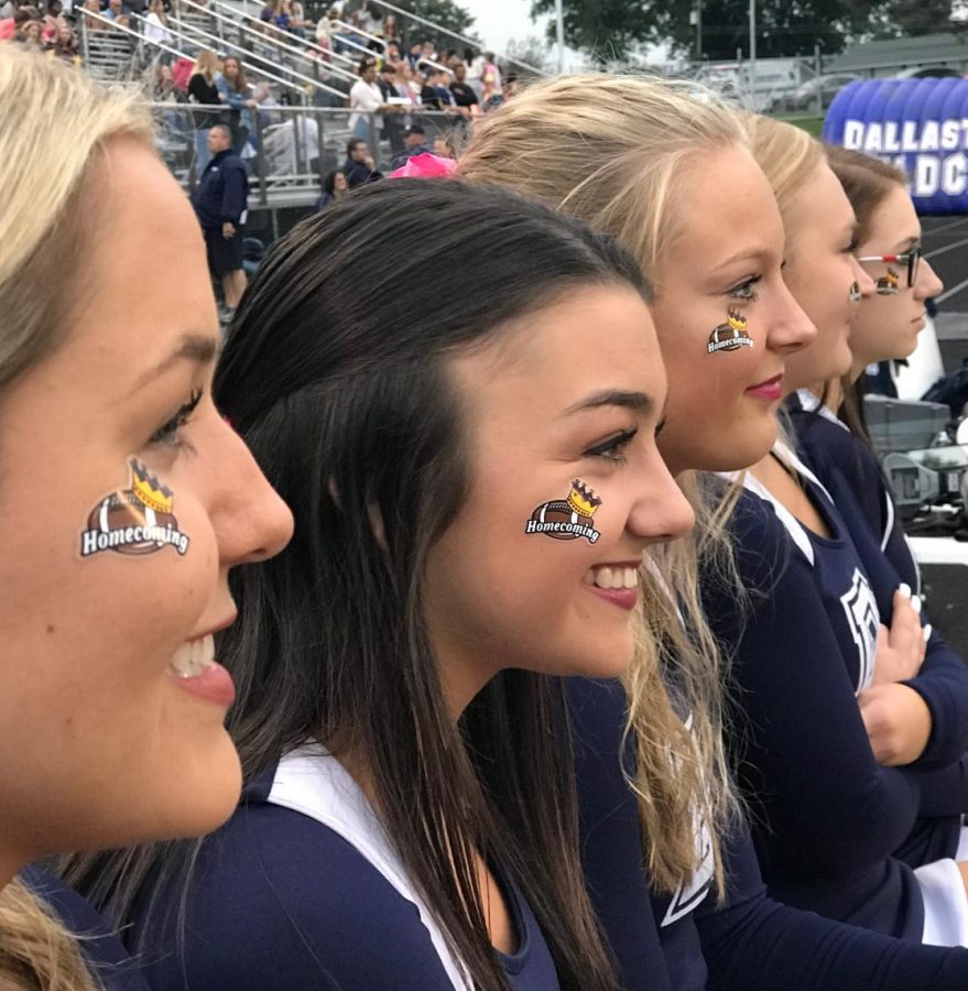 Senior cheerleaders watch the court members walk across the field before the annual Homecoming football game. 