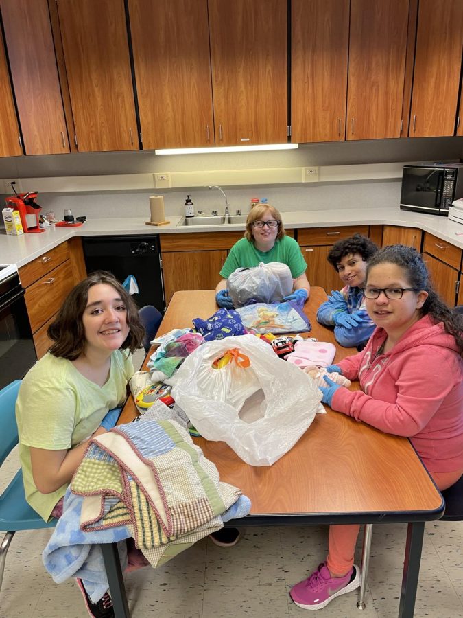 Four of the life skills students working together to sort the bags of donated clothes, toys, and other goods. Once the bags are sorted, the items will be packaged and sent to the local Community Aid store.