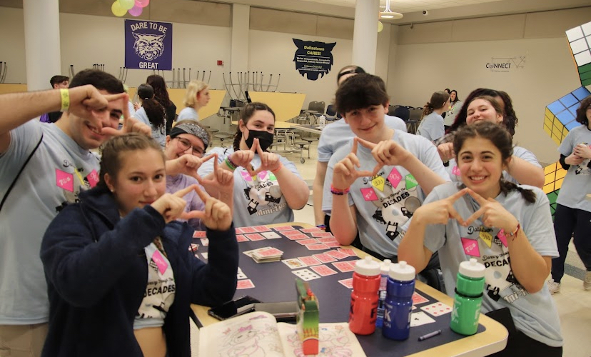 Students hold up the Four Diamonds symbol in the cafeteria while playing a card game. Hospitality brings lots of board games so people can play while they eat!