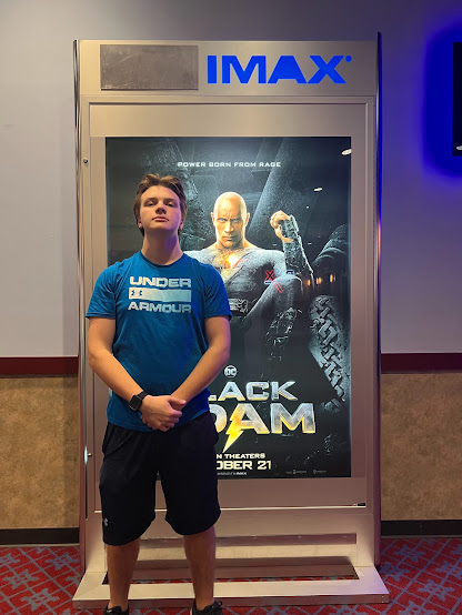 Jayden Huncher stands infront of the "Black Adam" poster  at RC Theatres at Queensgate.