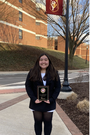 Olivia Lowry holding up her Lincoln-Douglas Debate state champion plaque outside of Bloomsburg University.