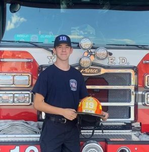 Klingenmaier proudly stands in front of a fire engine and presents his firefighting helmet. This has been a lifelong dream which has become reality for Klingenmaier.