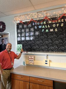 Business teacher Mr. Robinson poses in front of his Stock Market Wall of Fame. While Dallastown does not have an official class in stocks, students do learn some about it in several business classes. 