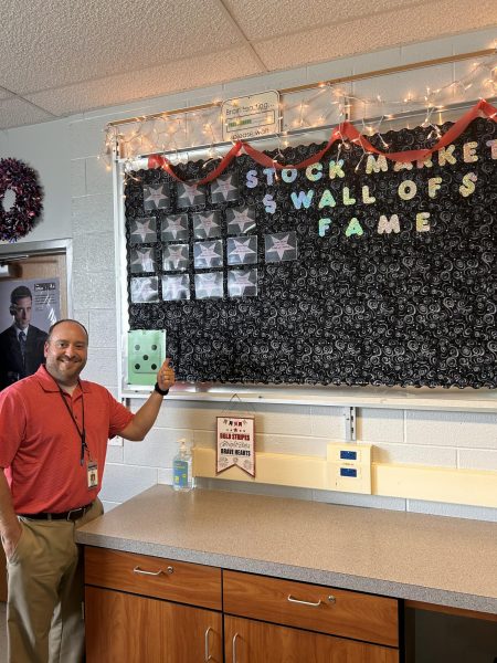 Business teacher Mr. Robinson poses in front of his Stock Market Wall of Fame. While Dallastown does not have an official class in stocks, students do learn some about it in several business classes. 