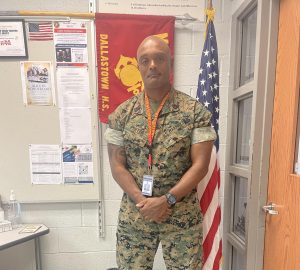 GySgt. Porter standing in front of the MCJROTC flag and the American flag in his and Maj. White's classroom.