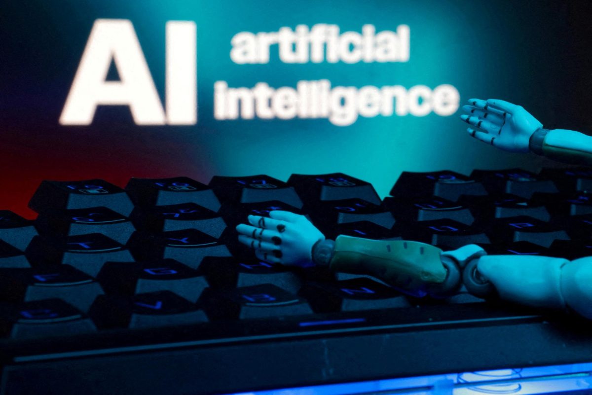 Artificial Intelligence is written on a computer screen with robot arms reaching towards it.