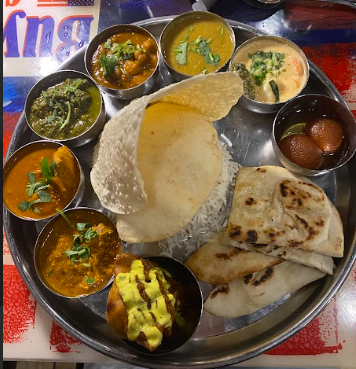 The thali dish including many samples of curries and a samosa.