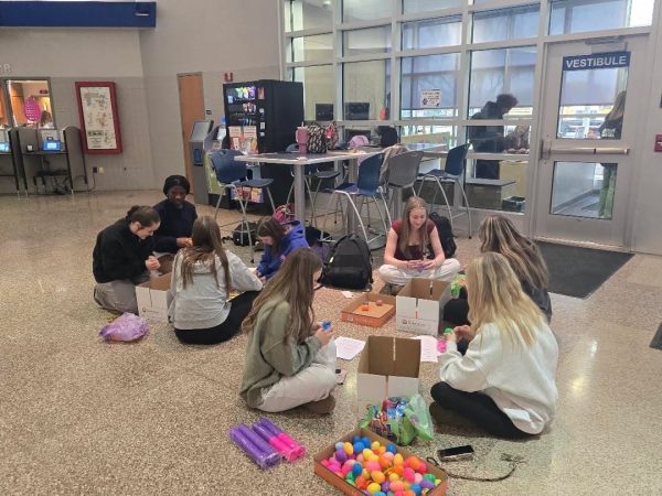8 female circles sitting around boxes of colorful plastic easter eggs, filling them with candy.