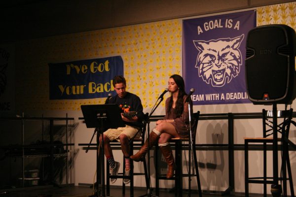 A boy and a girl sat on stage, performing a singing duet.