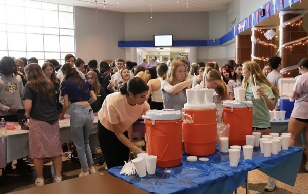 A large group of students huddled in the high school's lobby around long tables set up with food and drinks for purchasing.