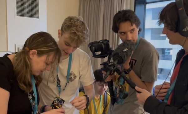 4 students from dallastown crowd as one holds a camera, each in the mist of reviewing footage of their work.