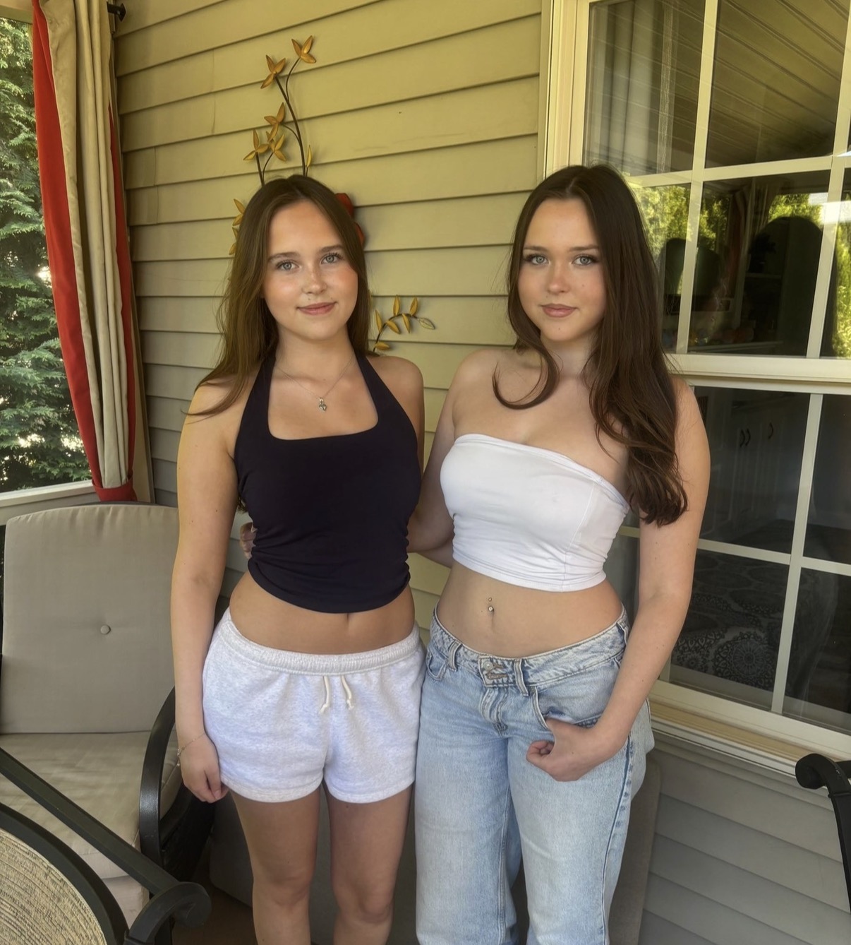 Two twin girls with brown hair stand next to each other smiling for a picture.