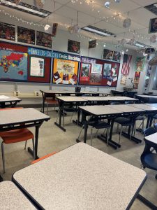 A classroom with colorful signs about different religions hanging on the walls with desks neatly set up in rows of three.