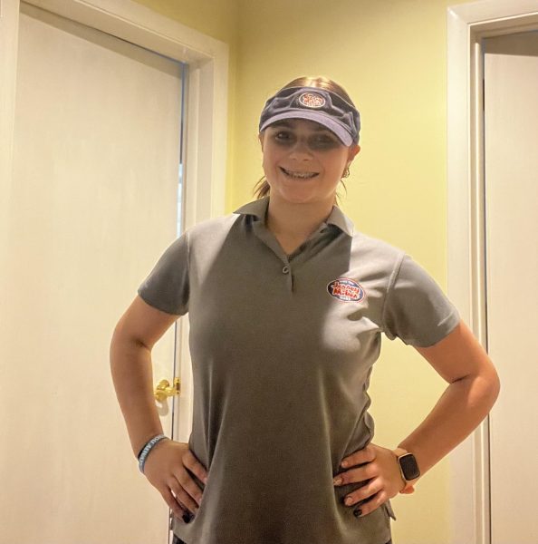 A girl in a gray top and blue hat with her hands on her hips smiling before going to work. 